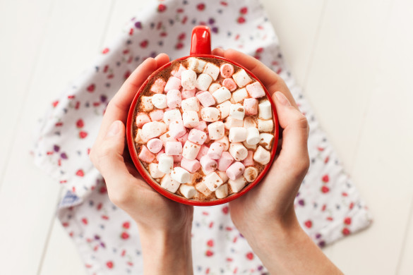 Hands holding hot chocolate with marshmallows in cup
